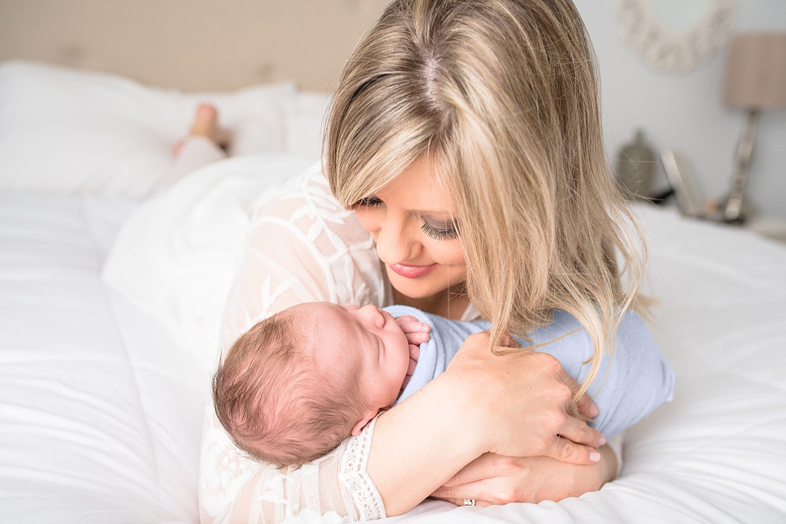 mom and baby boy, in home newborn photography in San Diego, baby boy wrapped in blue, lifestyle image of mom and baby on bed