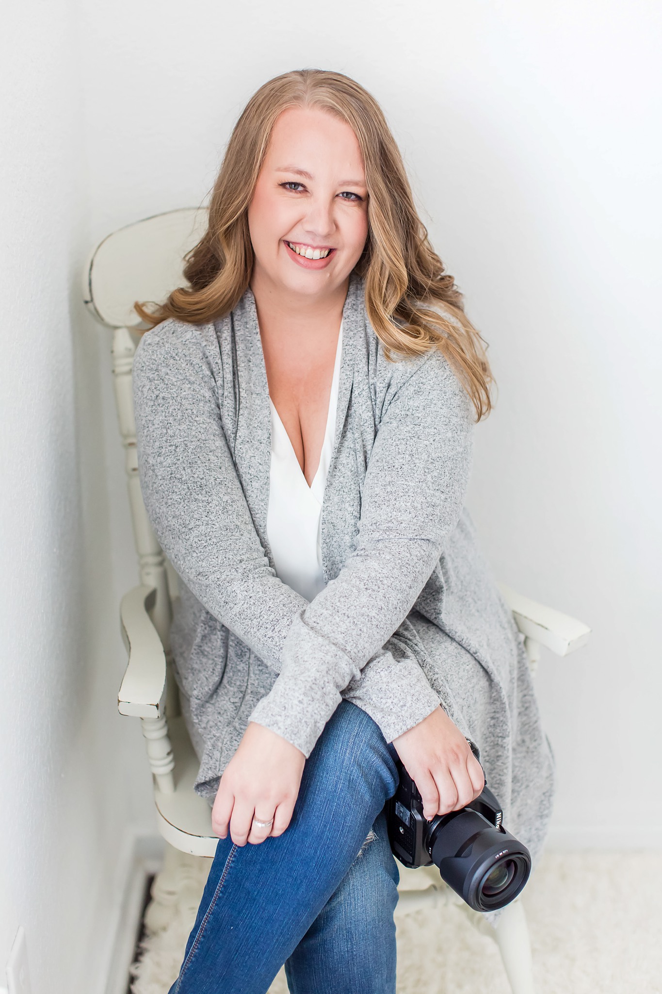 San Diego family & motherhood photographer sitting in a chair holding a camera smiling