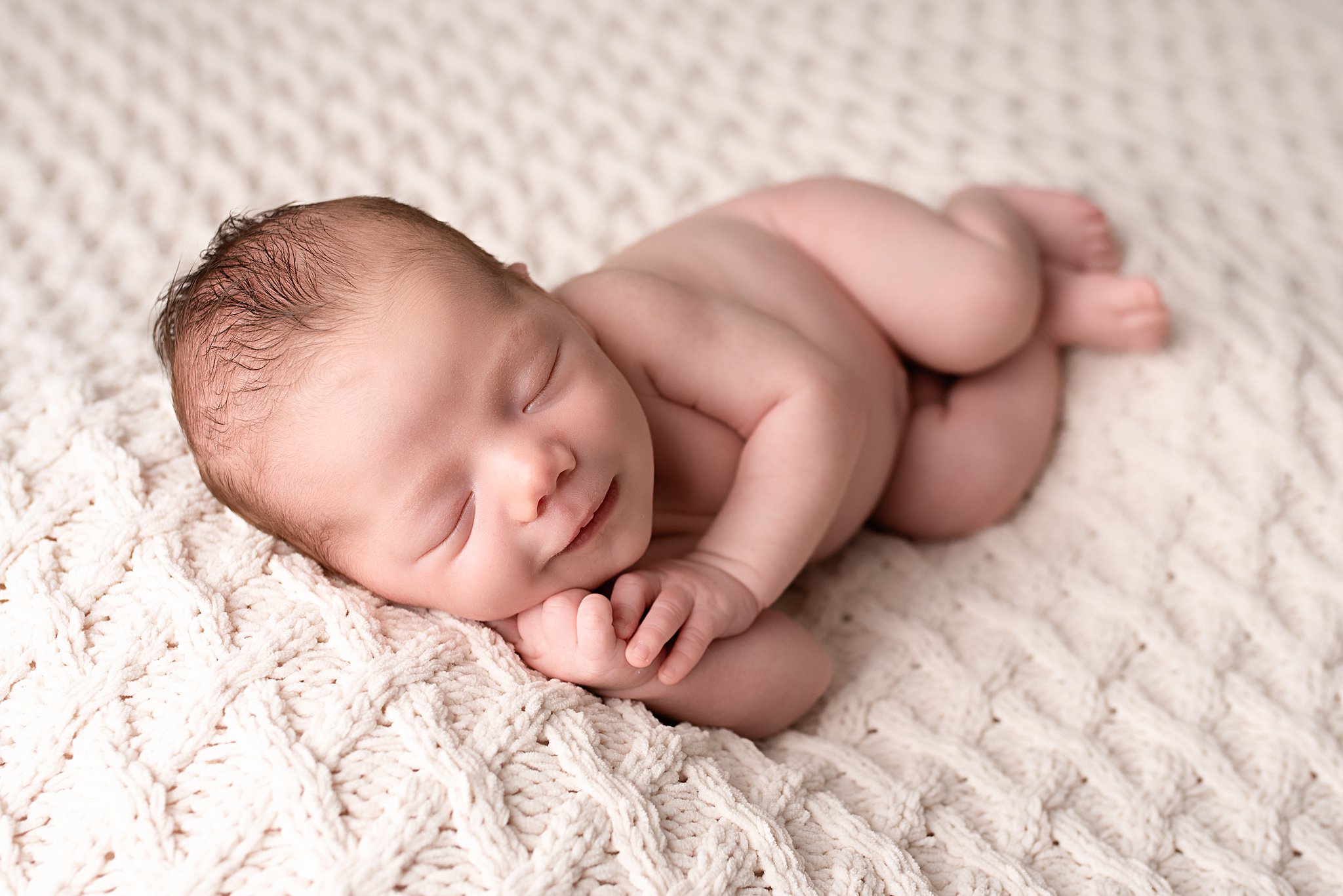 A newborn baby smiles in it's sleep on a woven blanket Blossom Baby Oceanside