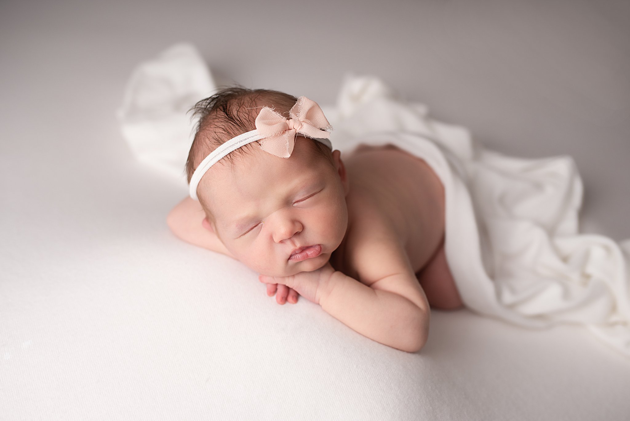 A newborn baby rests her head on her hands while wearing a pink bow headband san diego lactation consultant