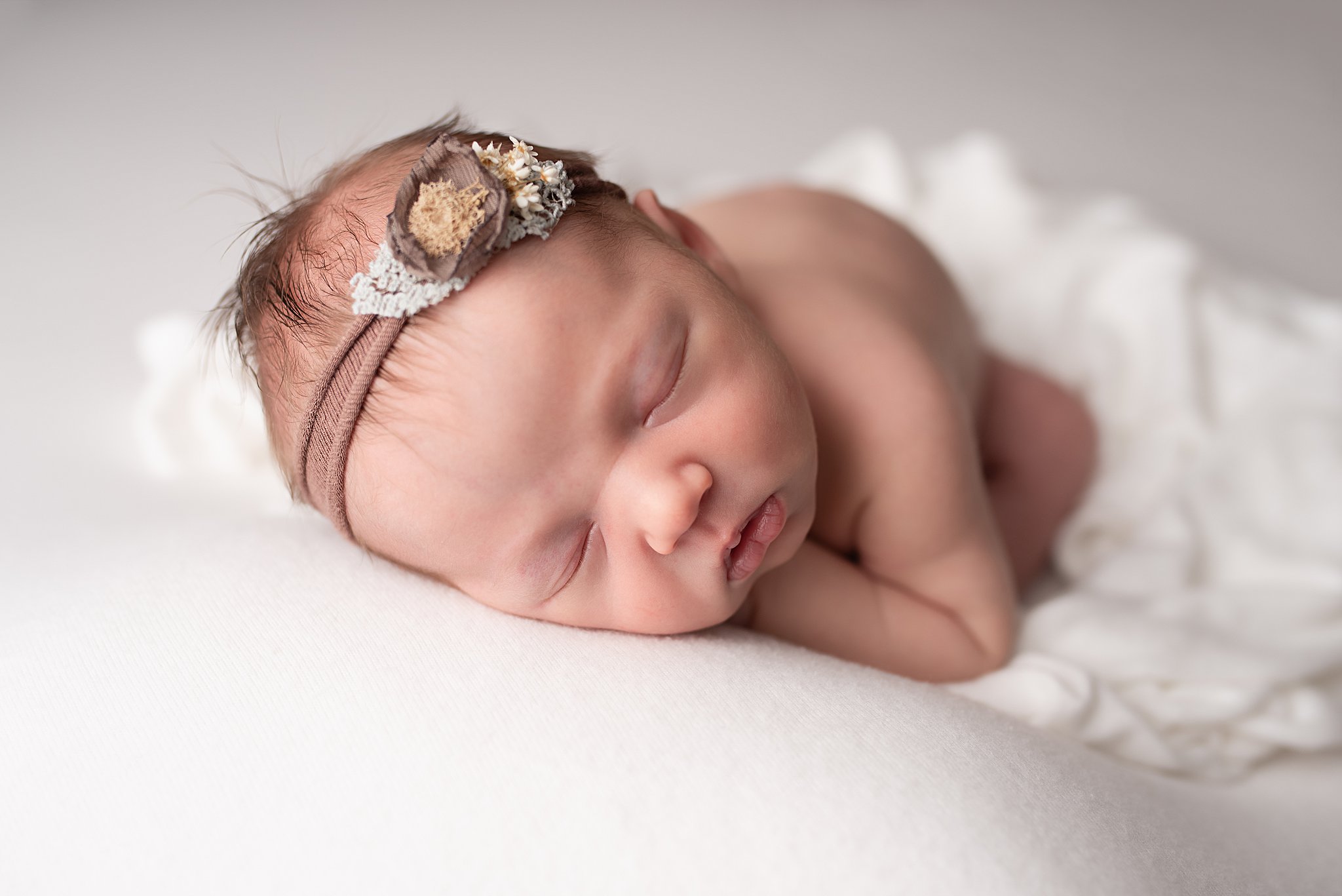 A newborn baby sleeps on a white bed in a fabric headband san diego lactation consultant