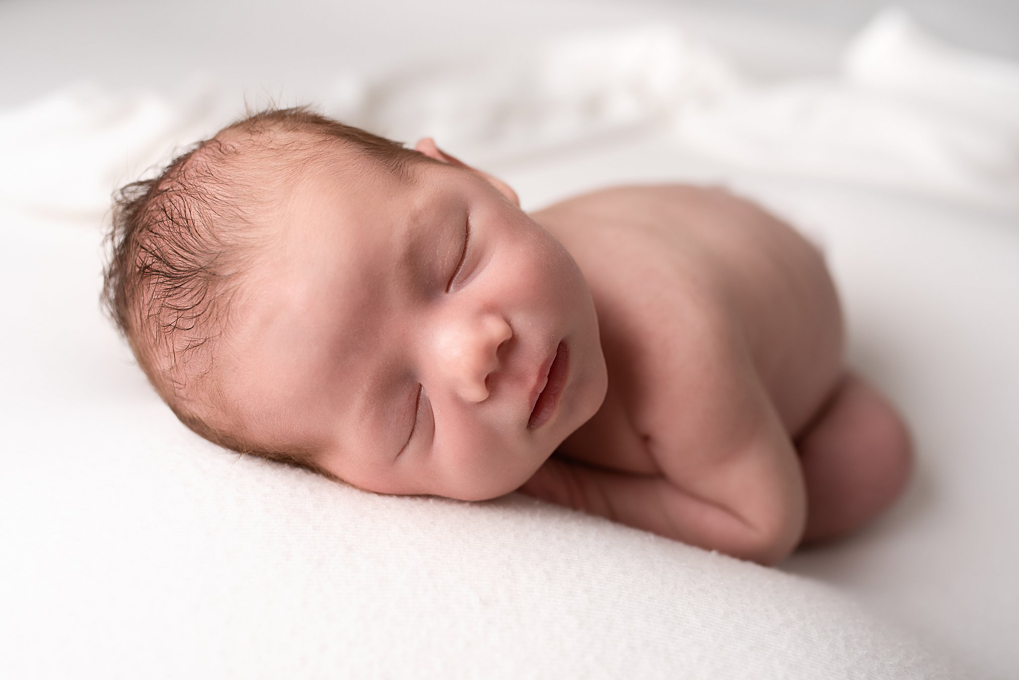 A newborn baby sleeps naked on a white bed san diego postpartum doula