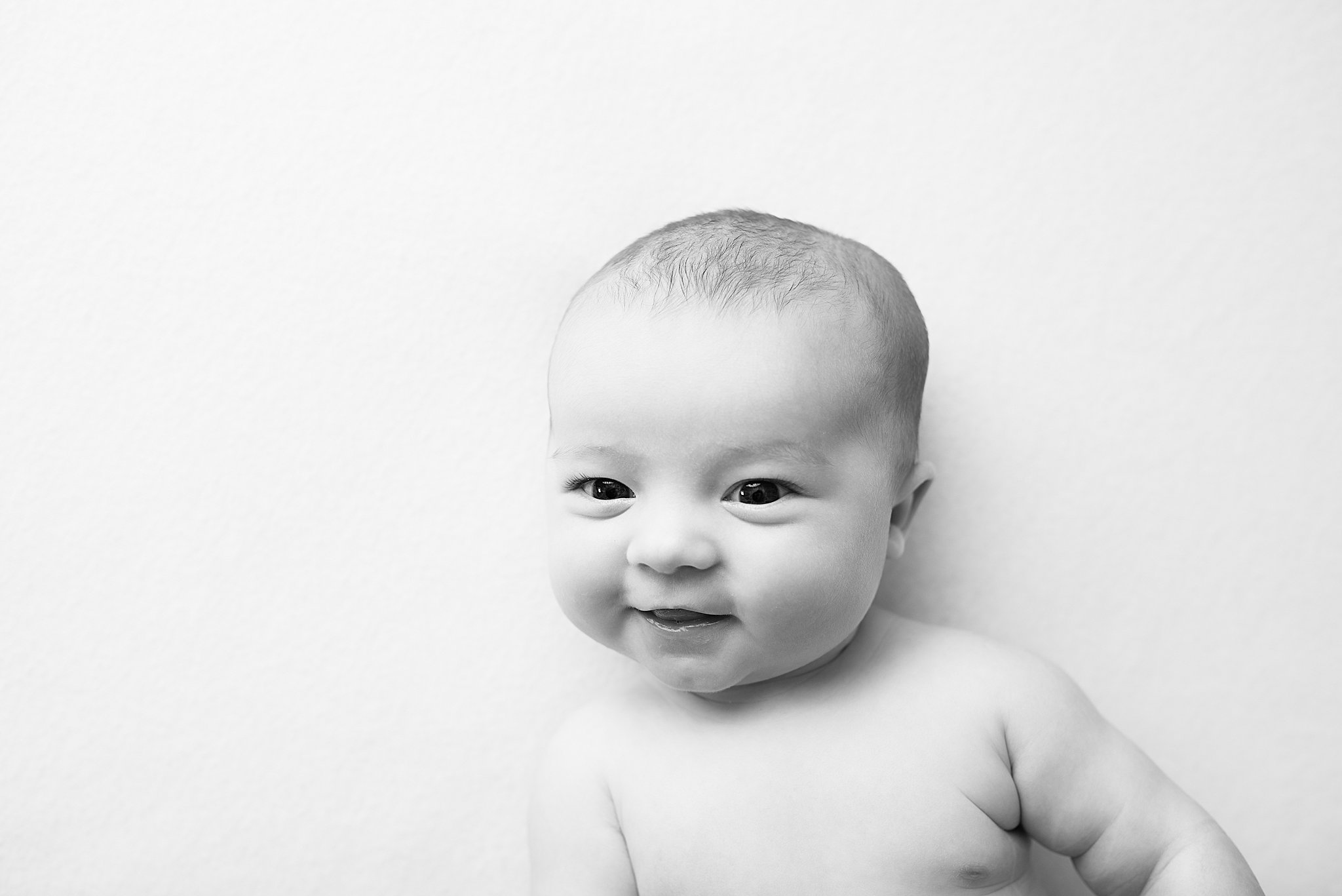 Details of a newborn baby smiling while laying on a white bed infant massage san diego