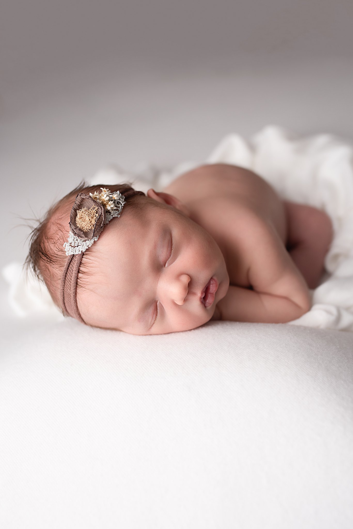 A newborn baby sleeps on a white pad in a headband san diego nannies