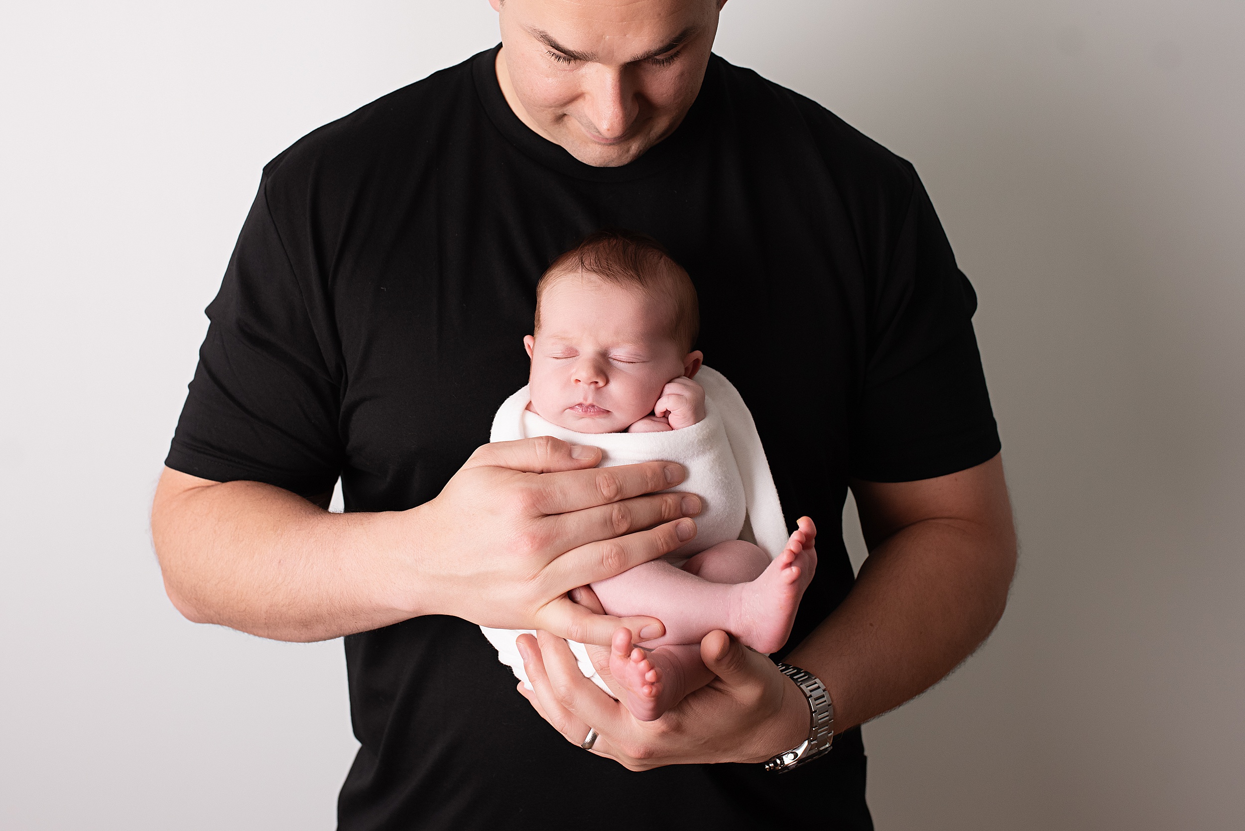 A new father in a black shirt holds his sleeping newborn sun against his chest san diego night nanny