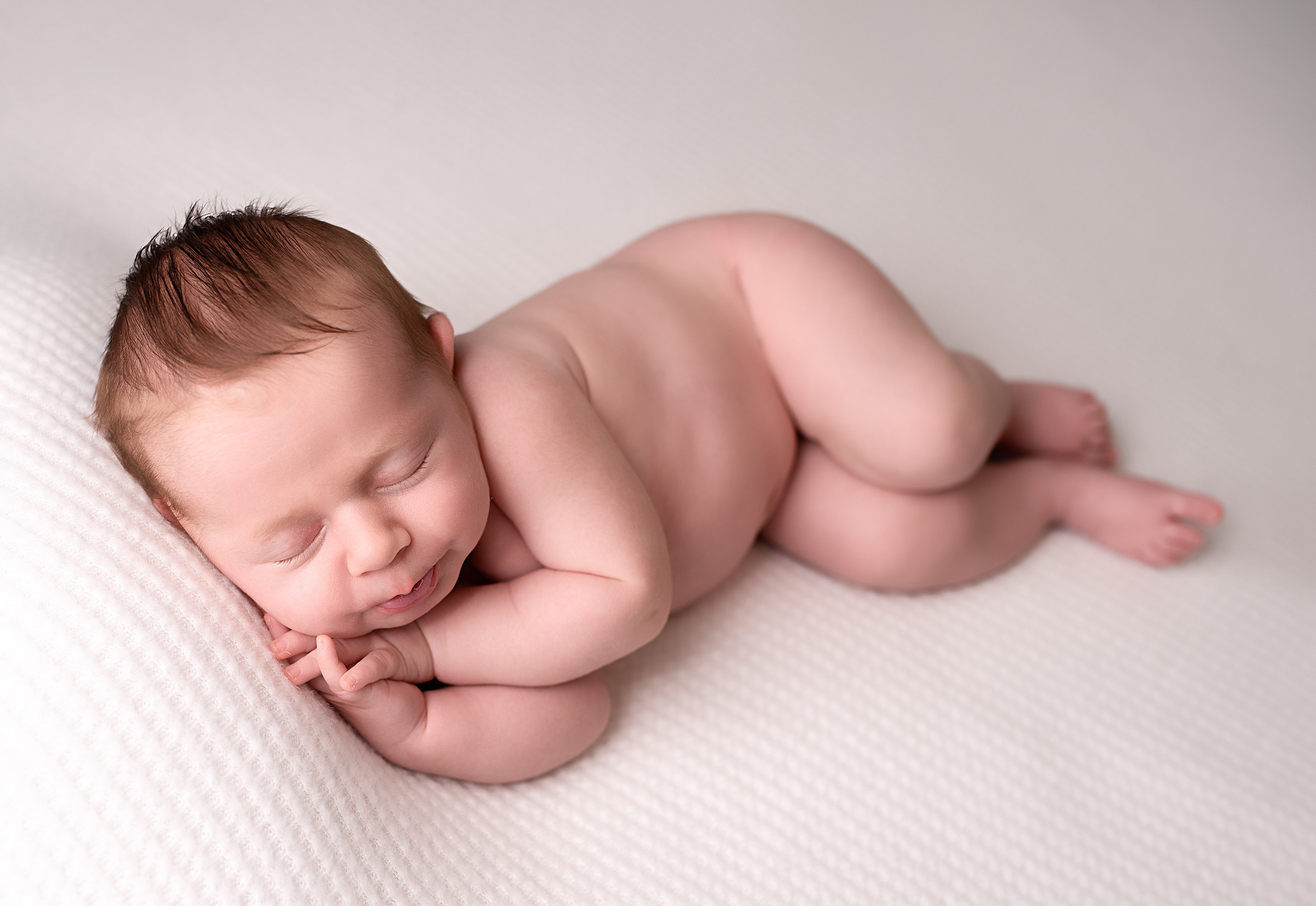 A newborn baby sleeps on its side naked on a white bed san diego night nanny
