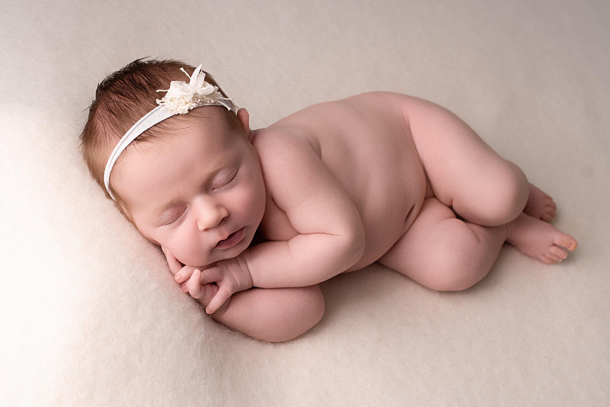 A newborn baby sleeps on its side while wearing a white headband baby furniture stores san diego