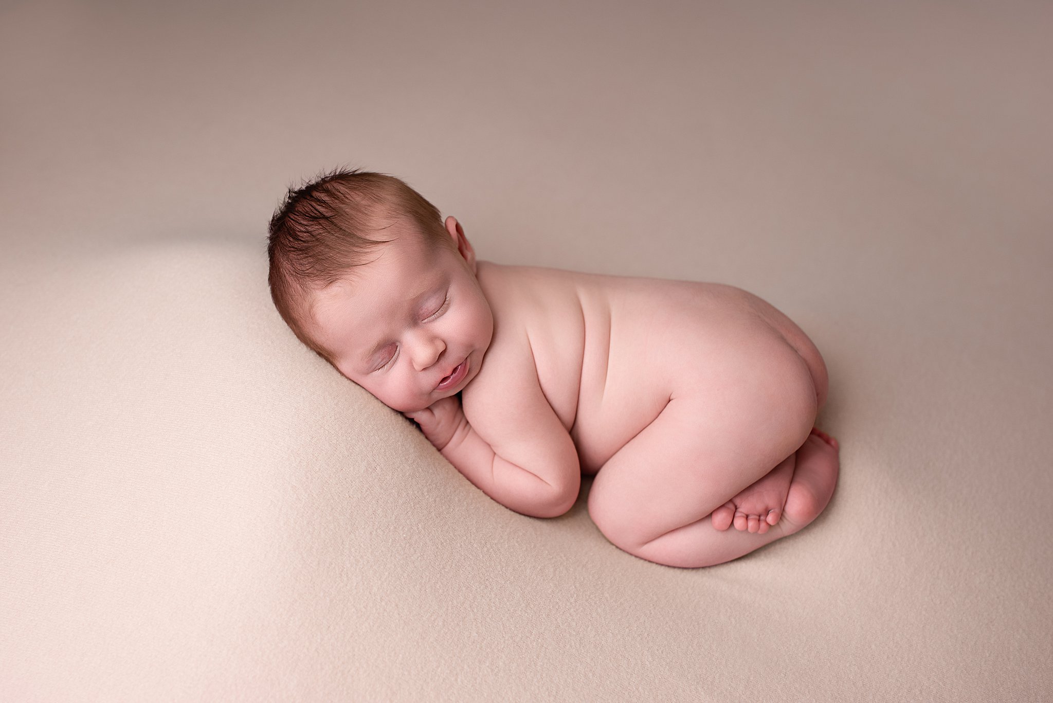 A newborn baby sleeps on a cream pad in a studio with help from north county doulas