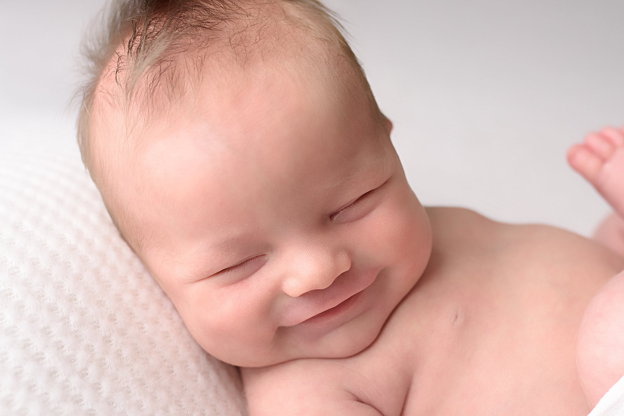 A newborn baby smiles in its sleep on a white pillow