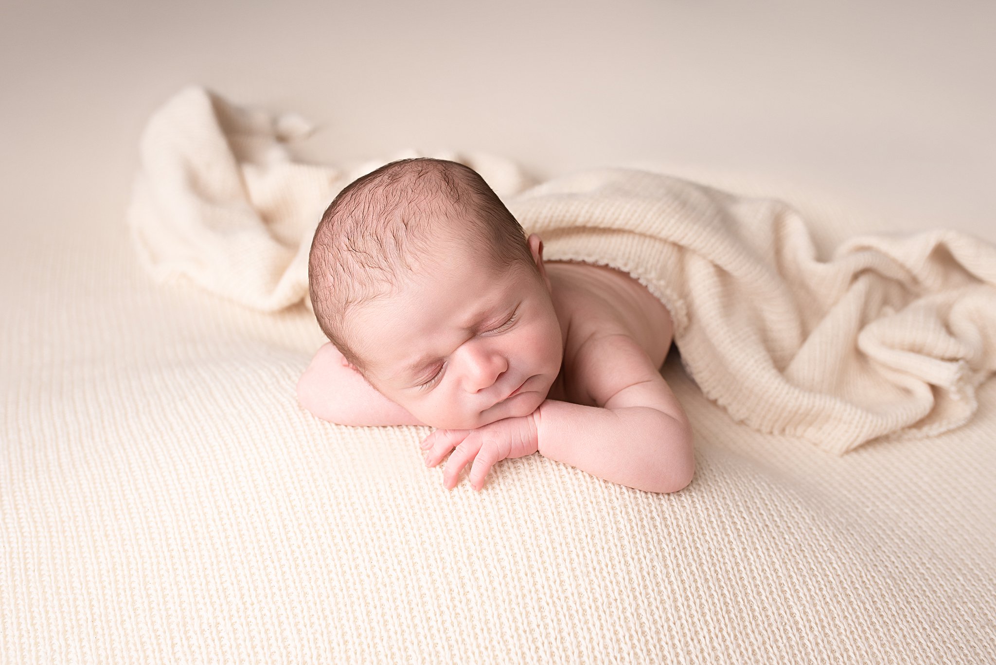 A newborn baby sleeps on its belly on a cream bed