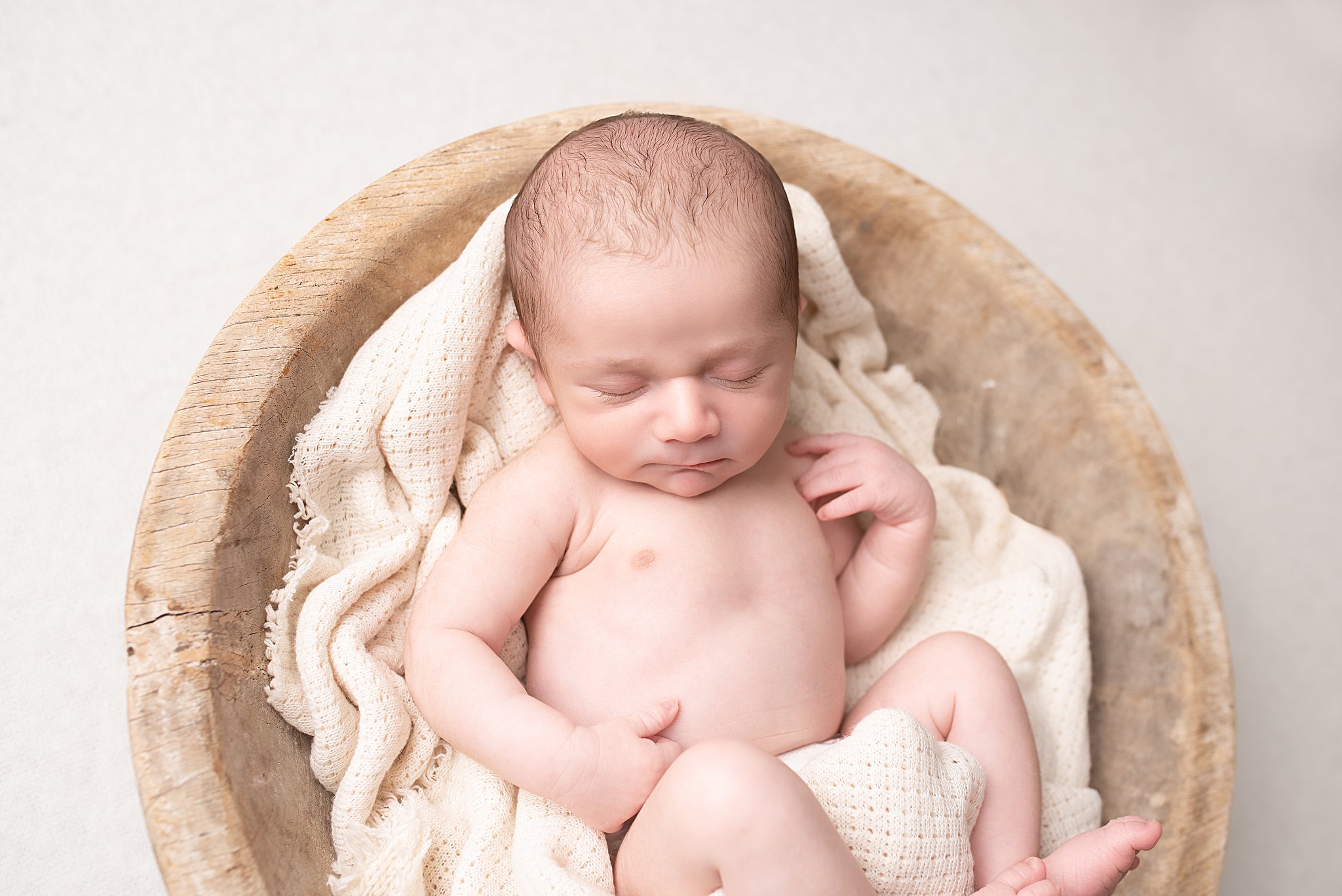 A newborn baby sleeps in a wooden bowl and blanket in a studio after san diego parenting classes